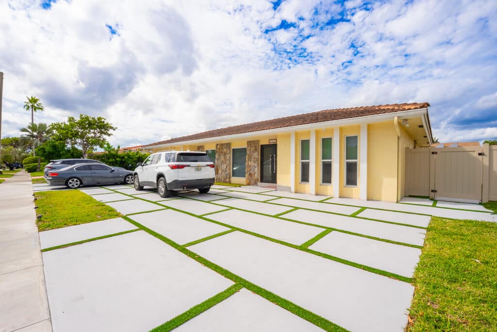 Wide concrete slab driveway with turf joints in front of a yellow single-story home