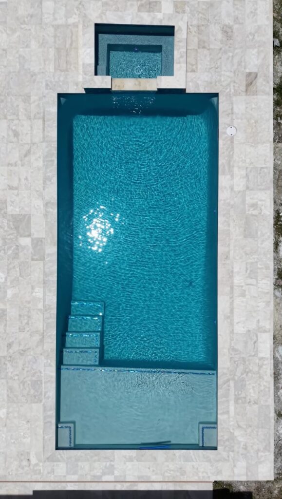 Top-down aerial view of a rectangular pool and spa with travertine deck