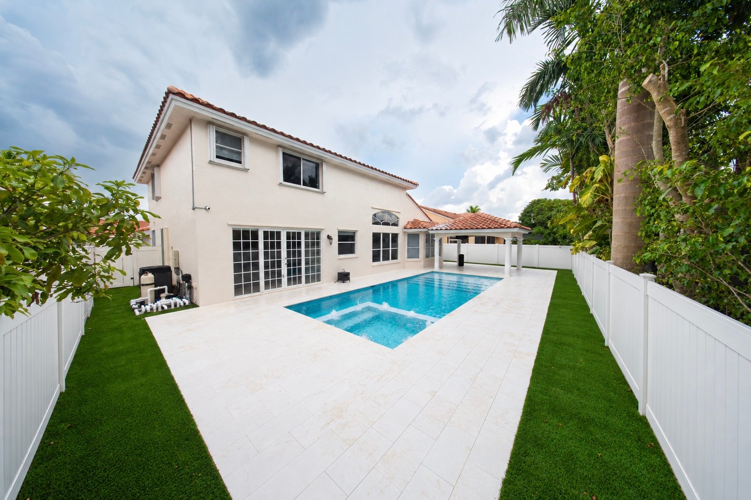 Pool and spa with a light stone deck behind a two-story home, the kind of pool remodeling Canet Group does in Palm Beach County