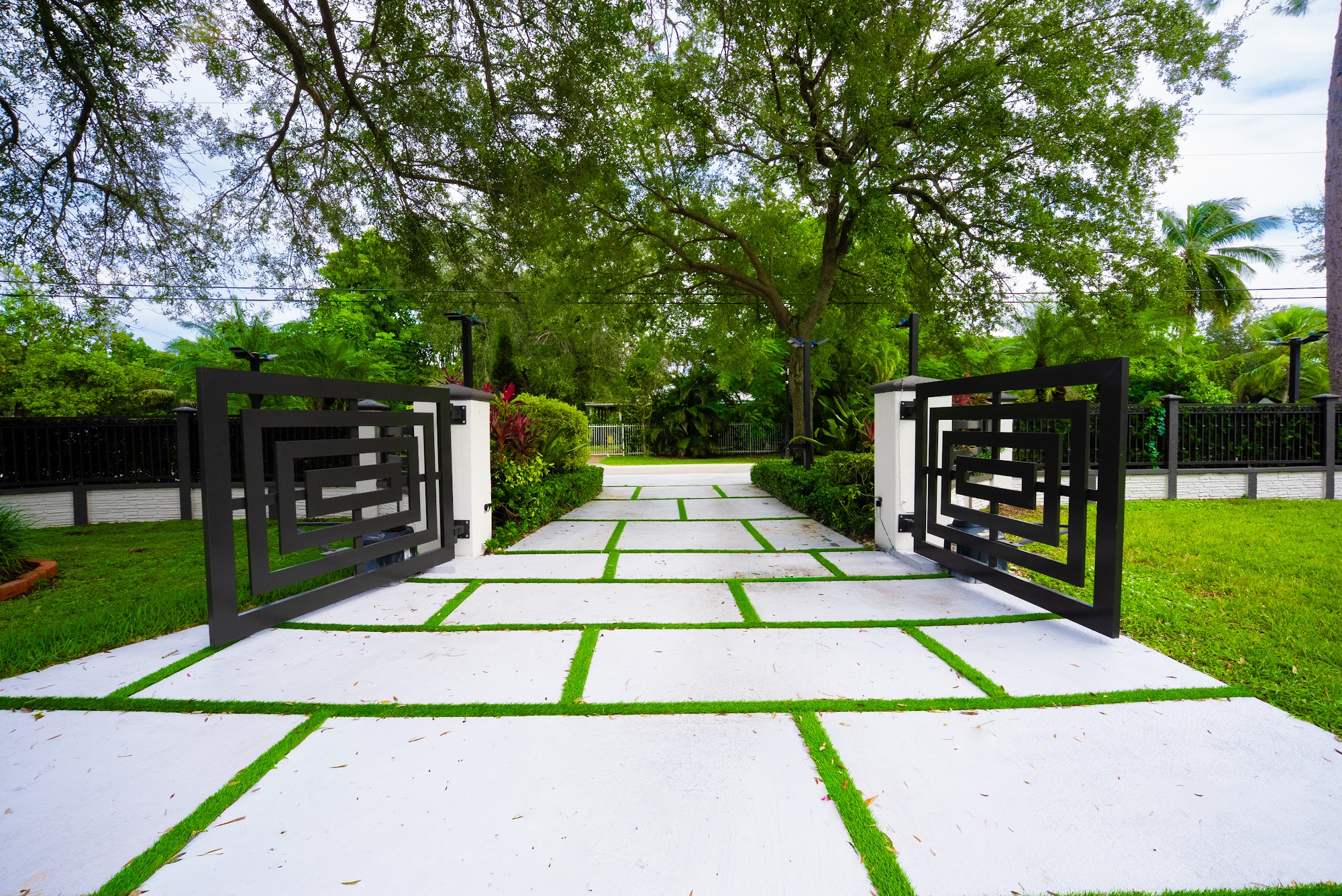 Wide concrete driveway slabs with turf joints leading to a black modern slat gate in Miami