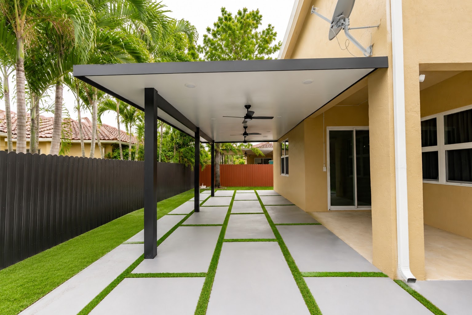 Covered aluminum patio, concrete walkway with turf joints and black privacy fence built by Canet Group in Miami Lakes