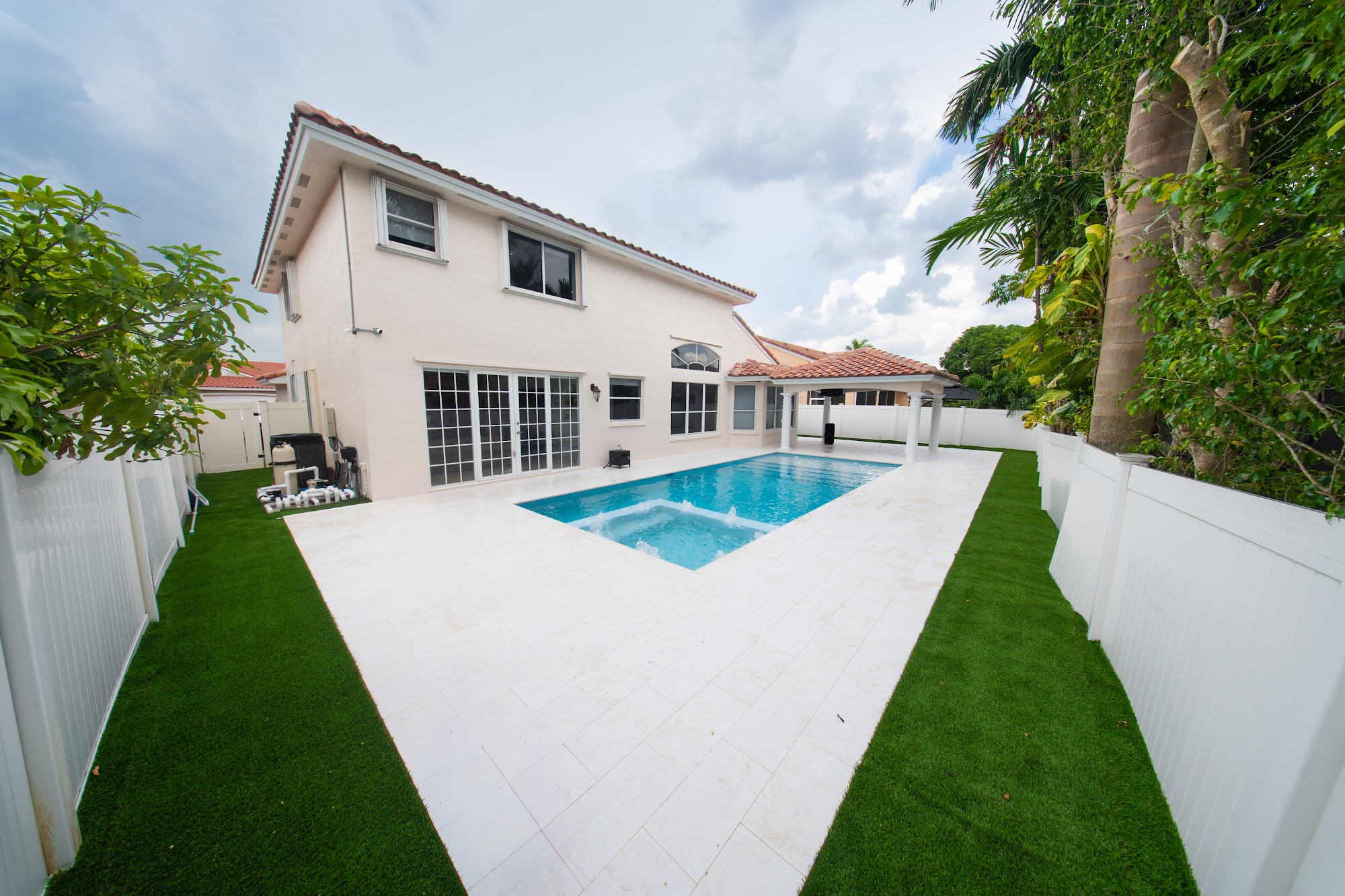 Renovated pool and spa with a white deck and turf borders behind a two-story home