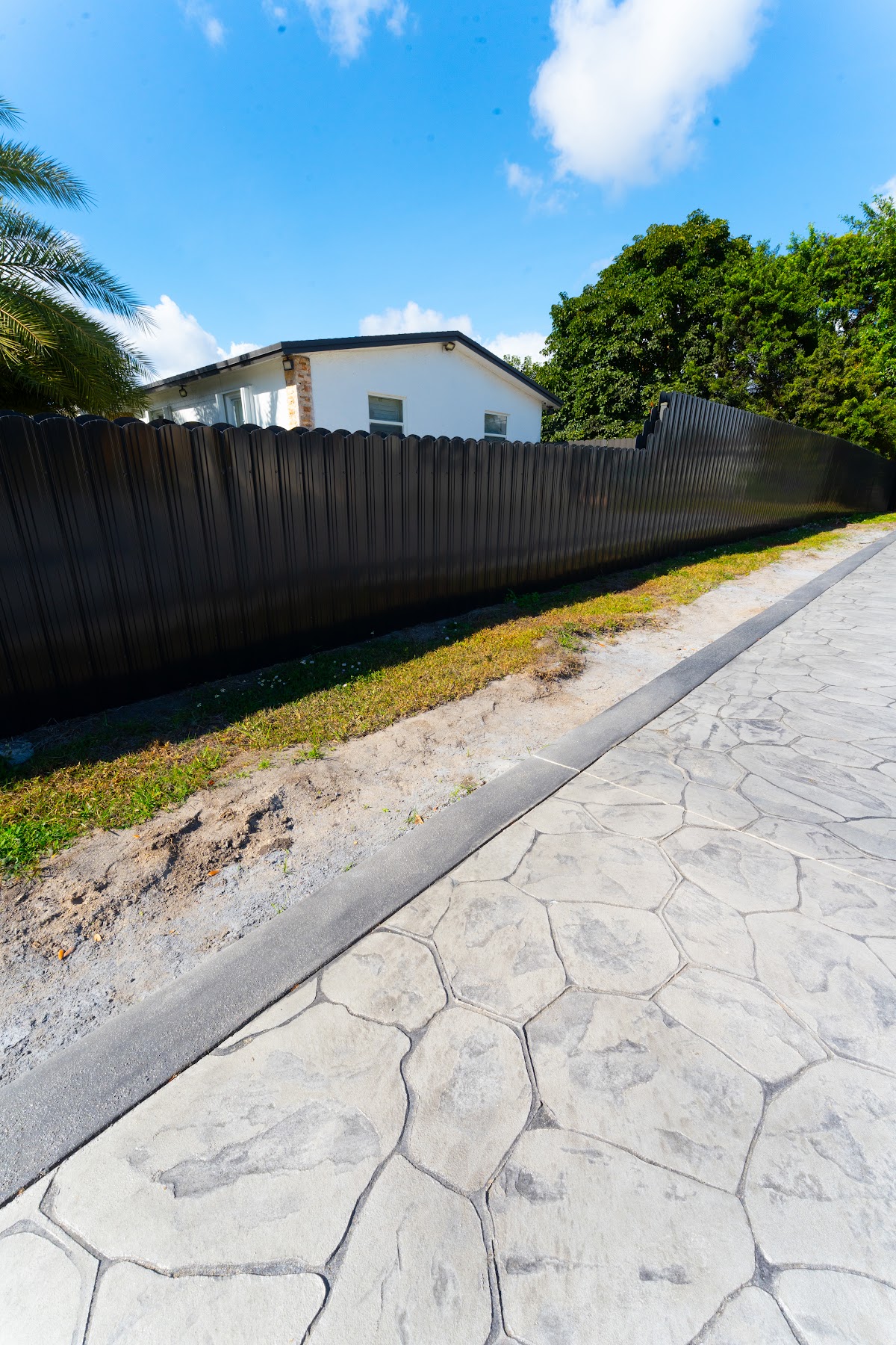 Long gray stamped concrete driveway with a stone pattern along a black fence, installed by Canet Group