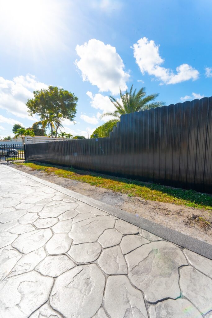 Close view of a stone-pattern stamped concrete walkway along a black fence, by Canet Group