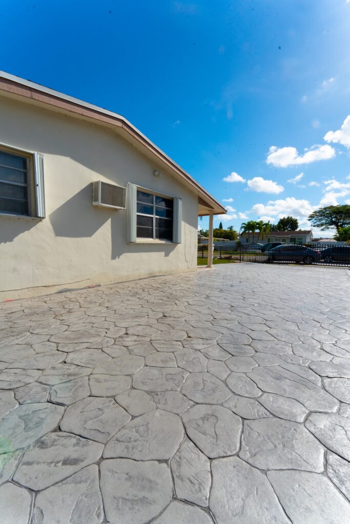 Gray stone-pattern stamped concrete beside a single-story home, by Canet Group