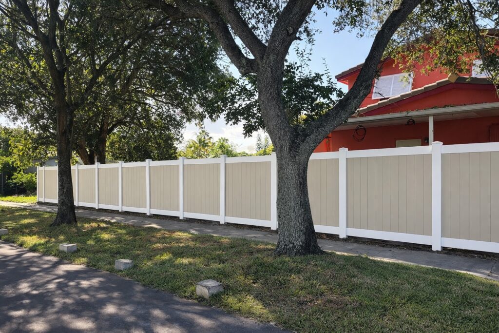 Tan vinyl privacy fence with white posts along a front yard and sidewalk in South Florida