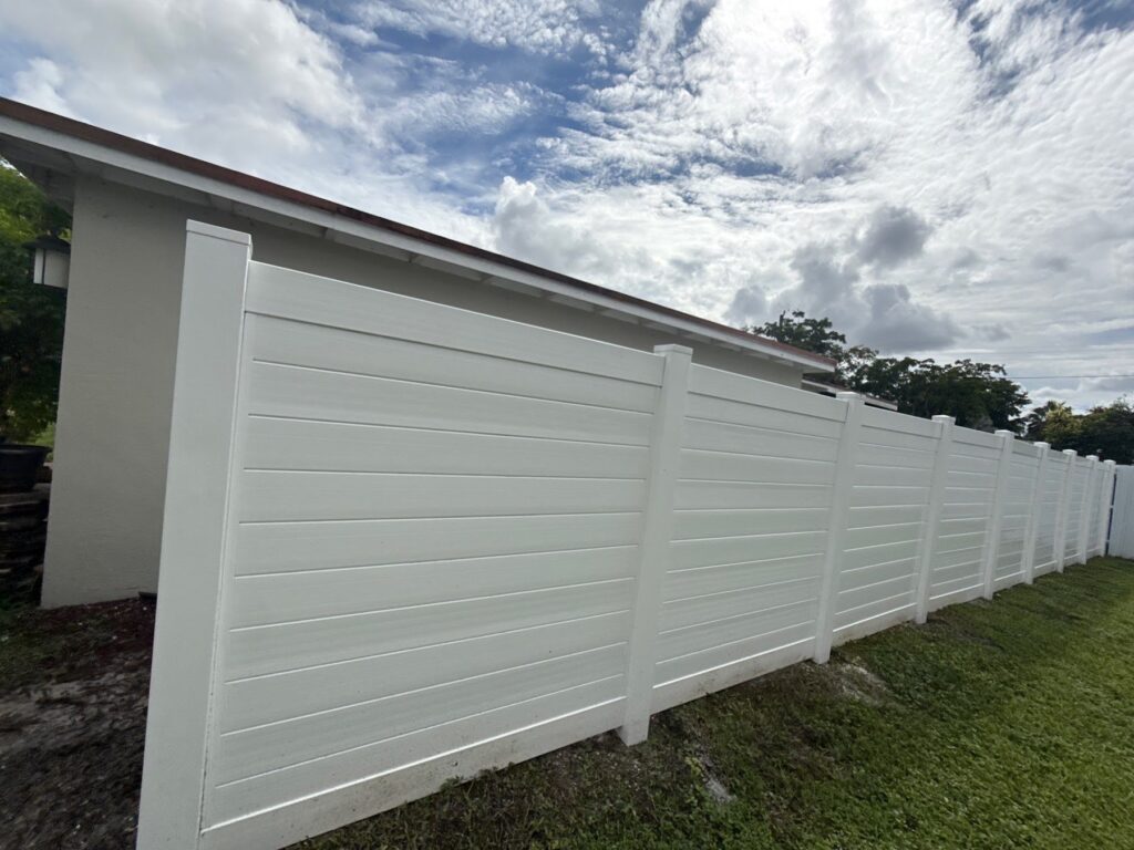 White horizontal vinyl privacy fence along a backyard lawn